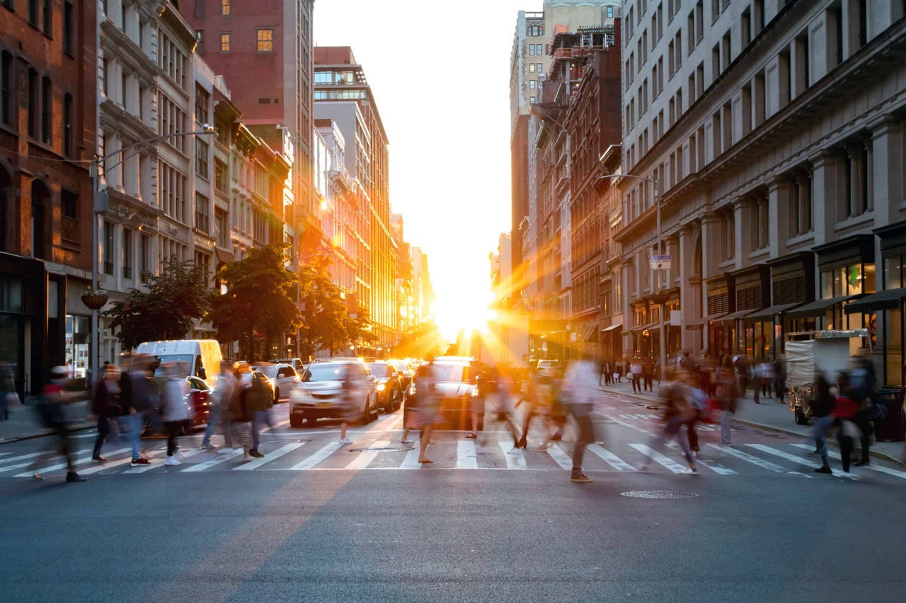 people crossing in the cross walk in a busy city during sunset