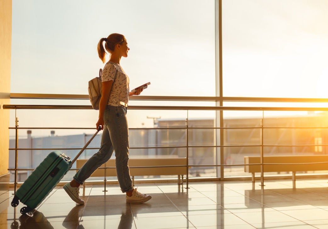 a woman walking through an airport pulling a rolling luggage case