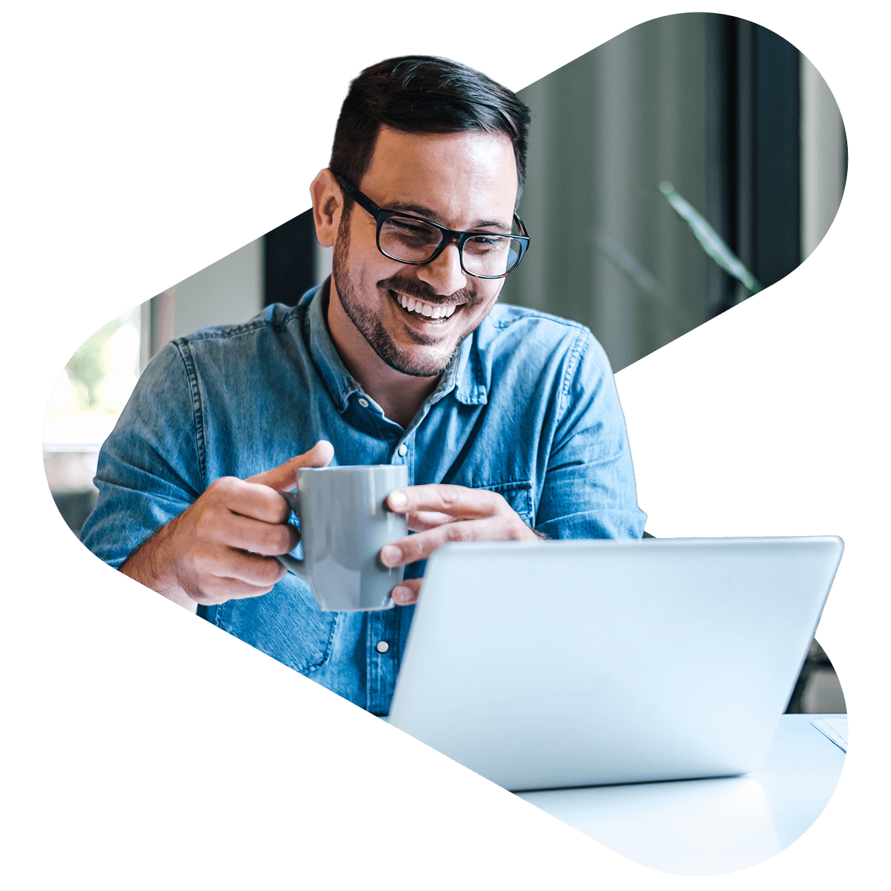 man at a laptop smiling while holding a mug