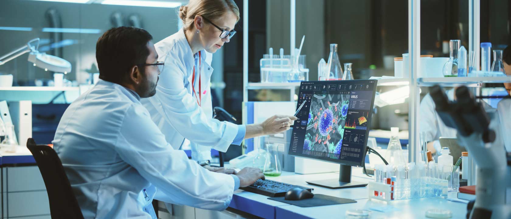 Photo of two researchers in white lab coats looking at health care imagery on a computer screen in a research laboratory.