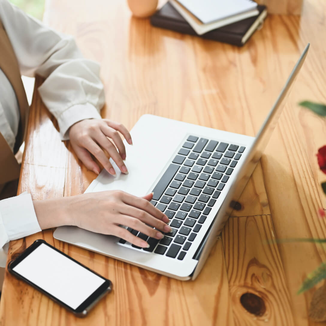 womans hands typing on laptop on desk with iphone next to her
