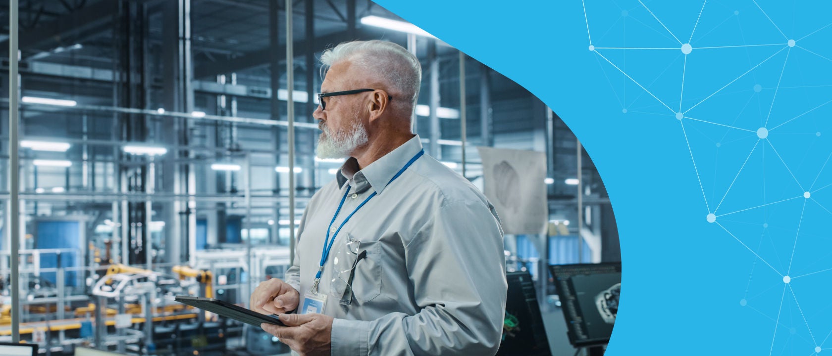 Man in a factory holding a tablet and looking out into the distance.