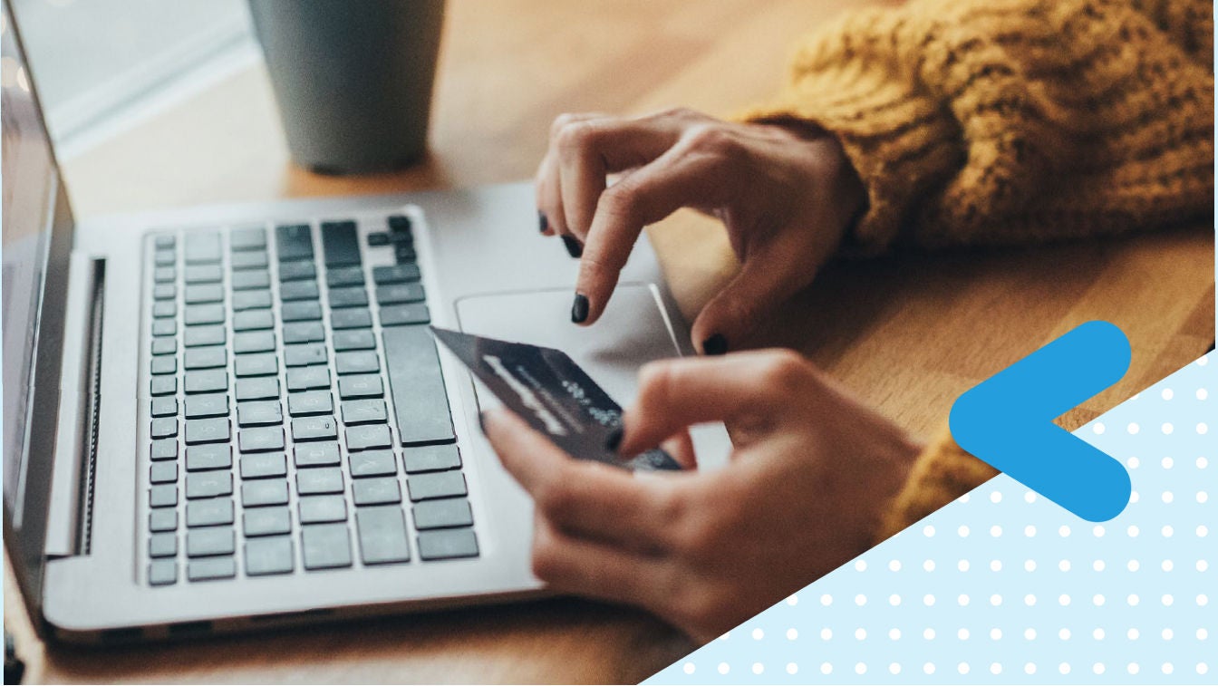 Open laptop on table, woman's hands holding a credit card typing in the number on the keypad