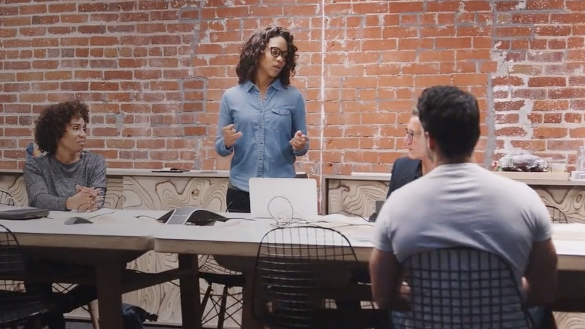 Conference room with 4 people meeting, brick wall in background