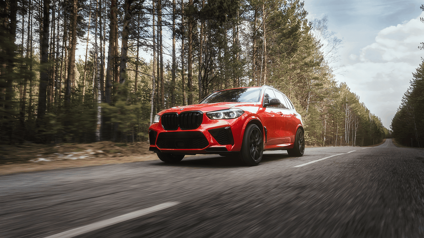 red bmw driving down the road with trees in background