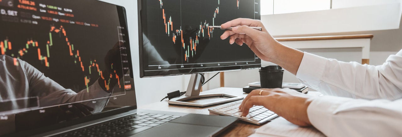 a hand with pen pointing at a screen showing financial charts