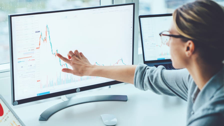 Business woman sitting at desk, pointing to graph on computer screen