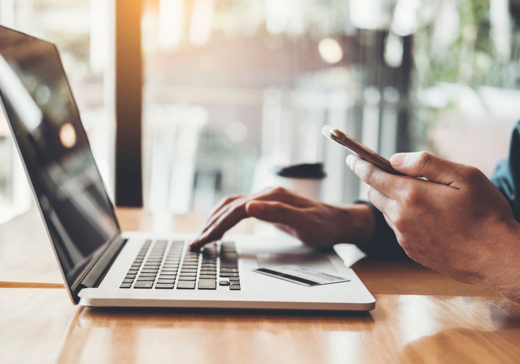 image of a hand resting on a laptop with a phone in the other hand